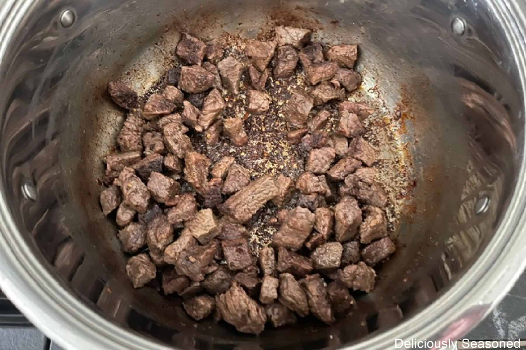 A pot of seared beef cubes with brown bits on the bottom.