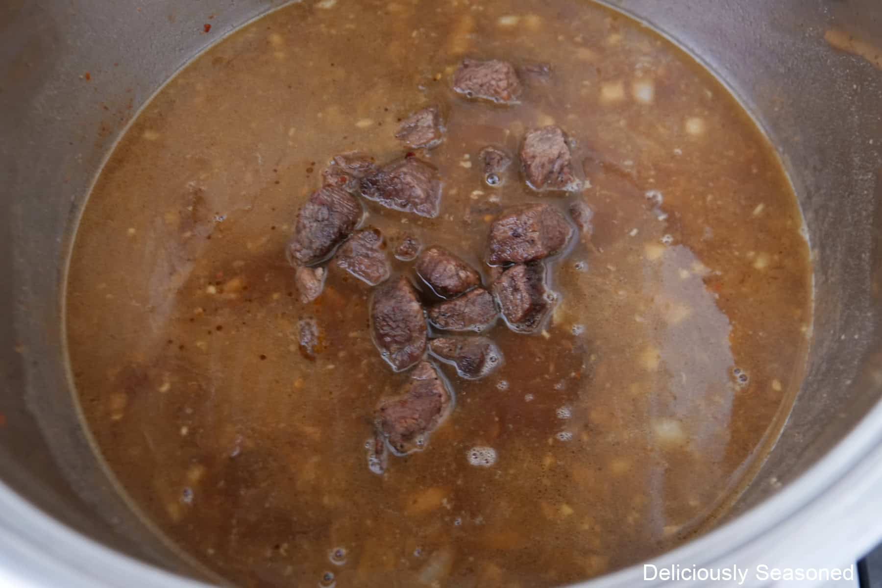 A pot with beef gravy and seared seasoned beef cubes added.