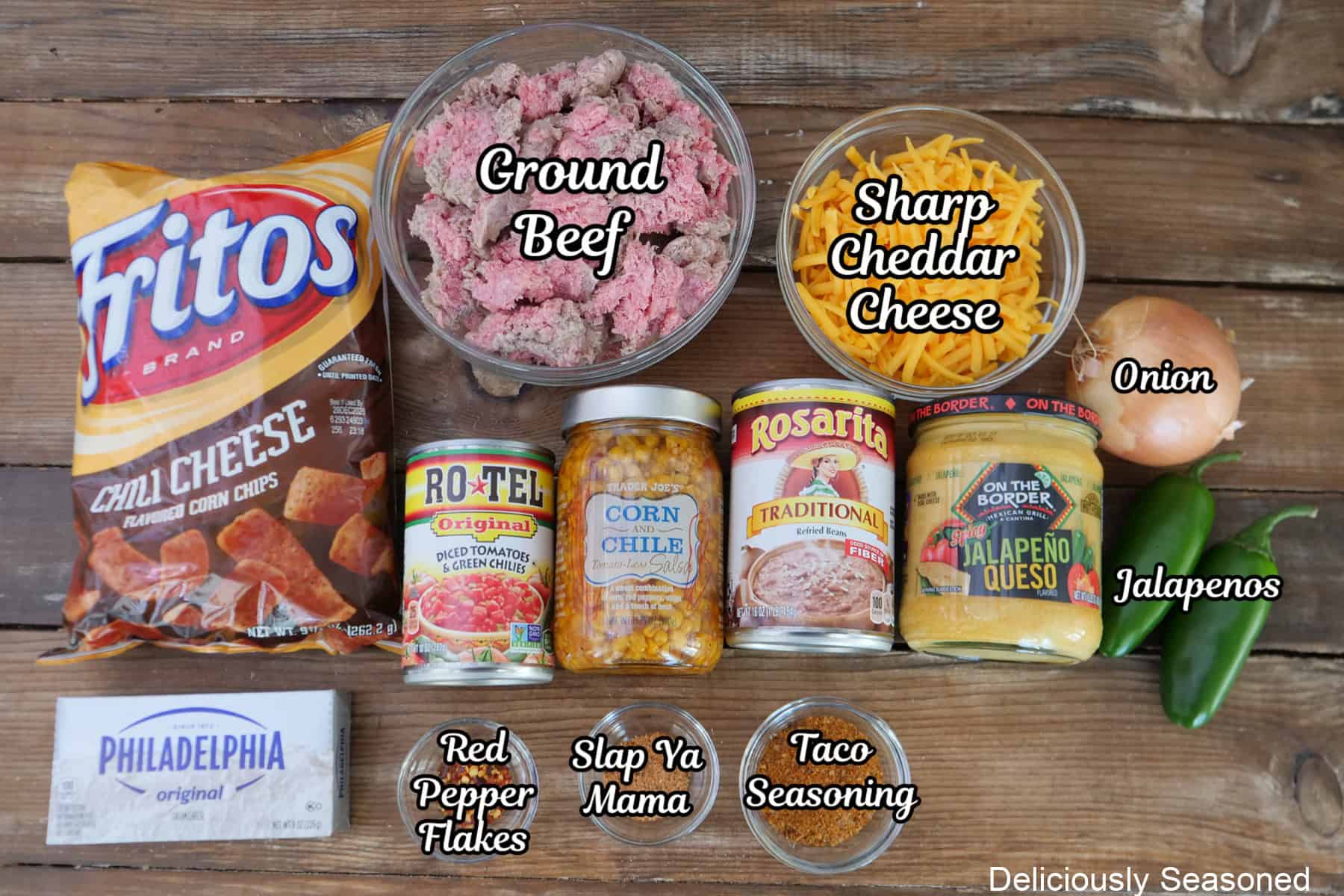 A rustic wood surface with all the ingredients placed on it to make cheesy queso taco dip.
