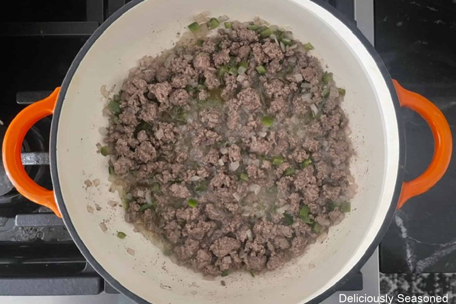 A frying pan with cooked ground beef, onions, and jalapenos in it.