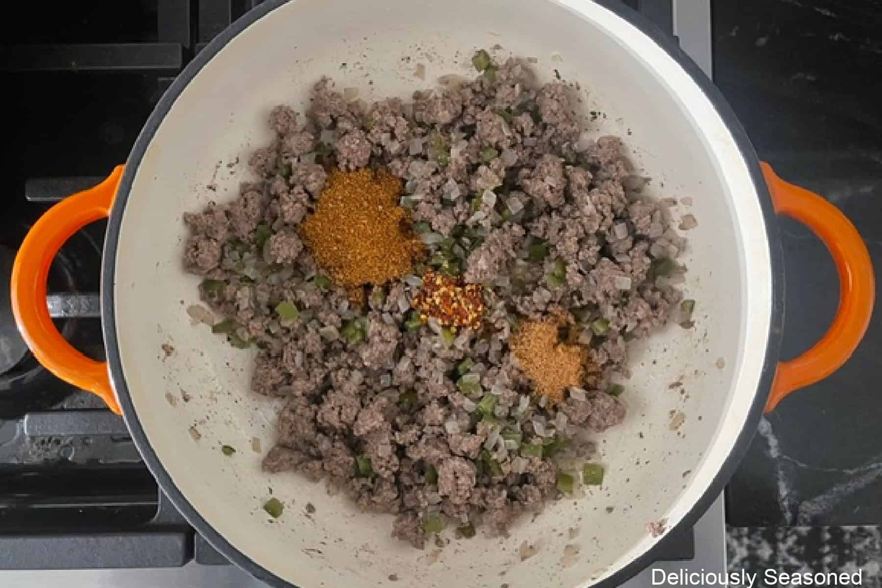 A pan with cooked ground beef, onions, jalapenos, and seasonings added on top.