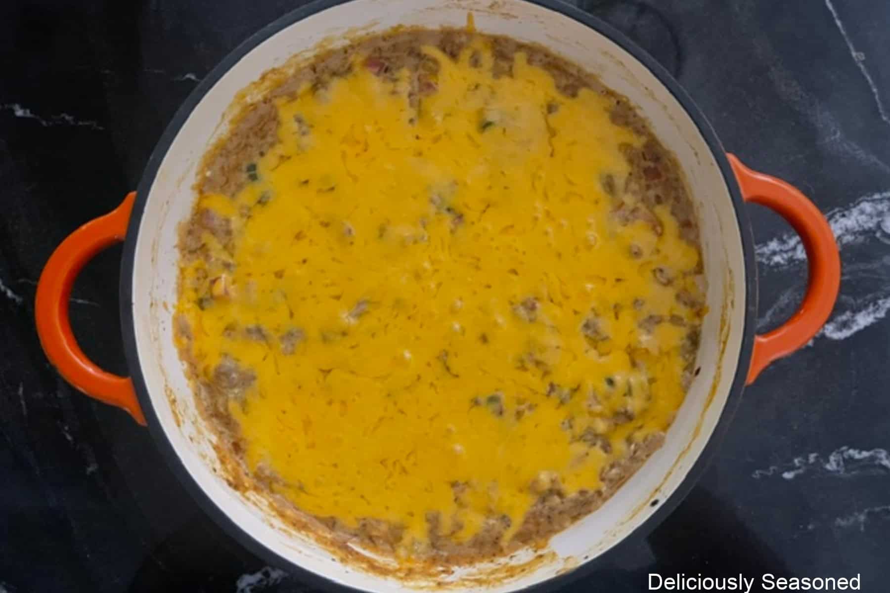 A pan with cheesy queso taco dip in it topped with melted cheese.