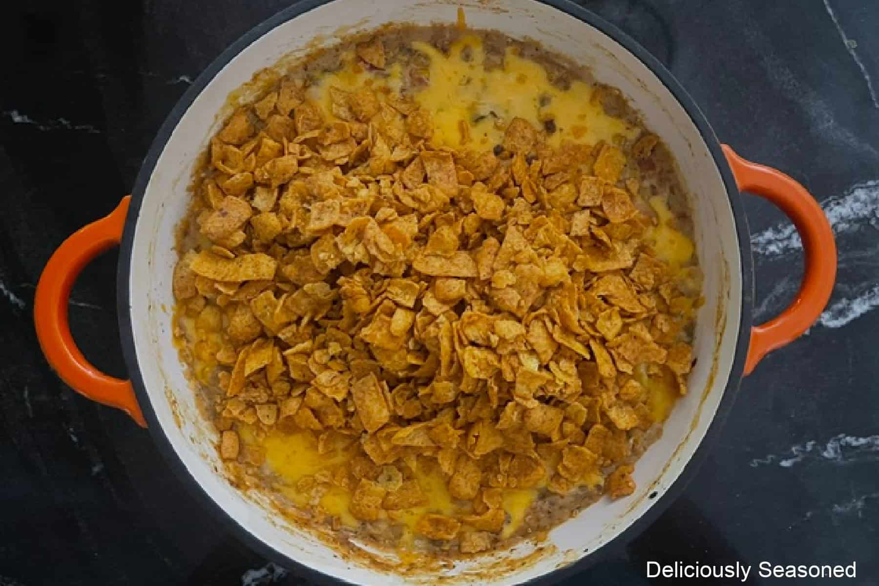 A pan with cheesy queso taco dip and coarsely crushed chili cheese Fritos added before being stirred together.