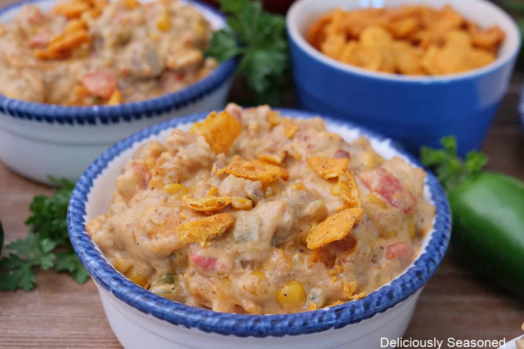 A white bowl with blue trim filled with a serving of cheesy queso taco dip with crunched up chili cheese Fritos added.