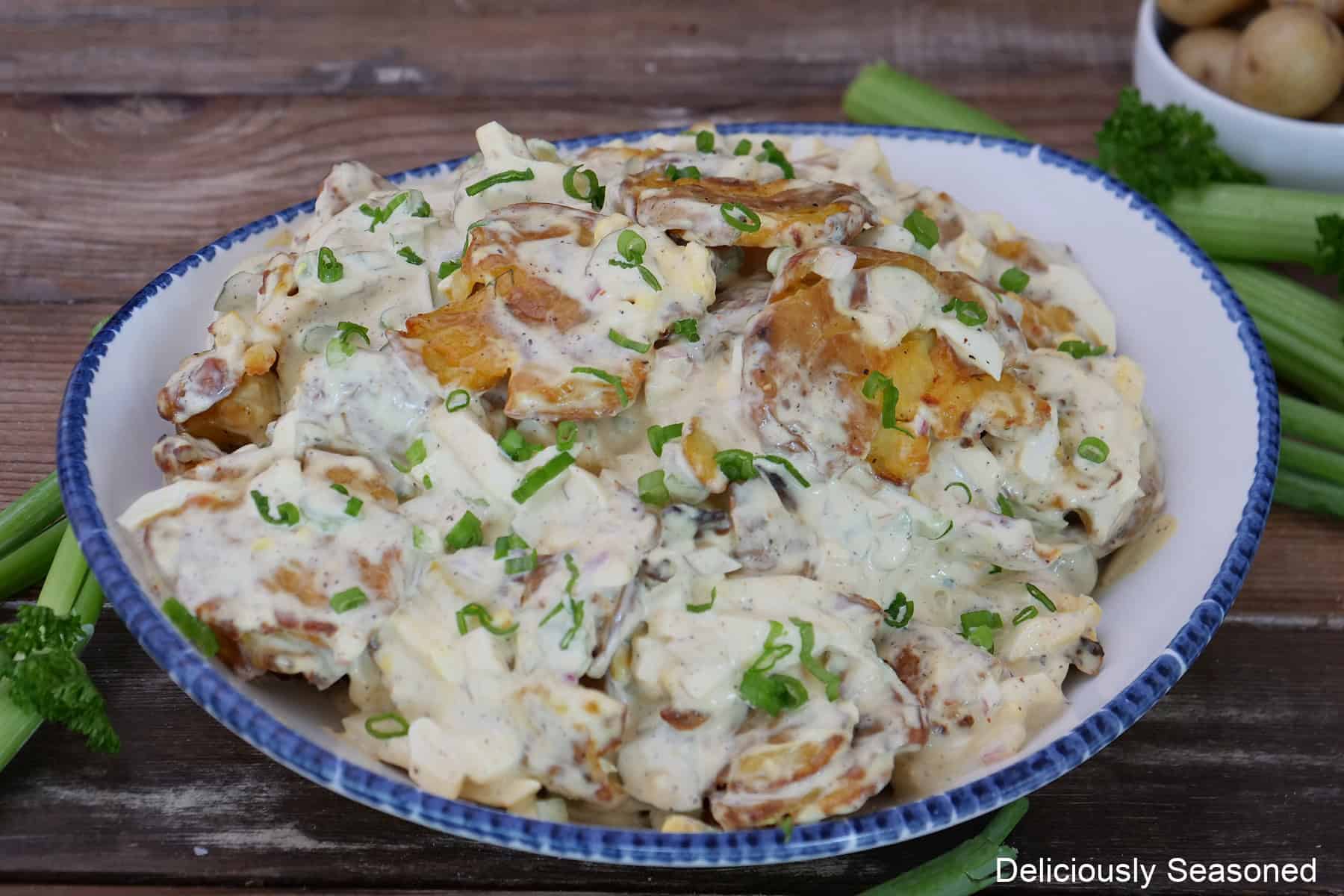 A white bowl with blue trim on a rustic wood surface with a serving of crispy potato salad in it.