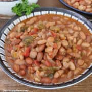 A bowl of crock pot spicy beans on a wood surface.