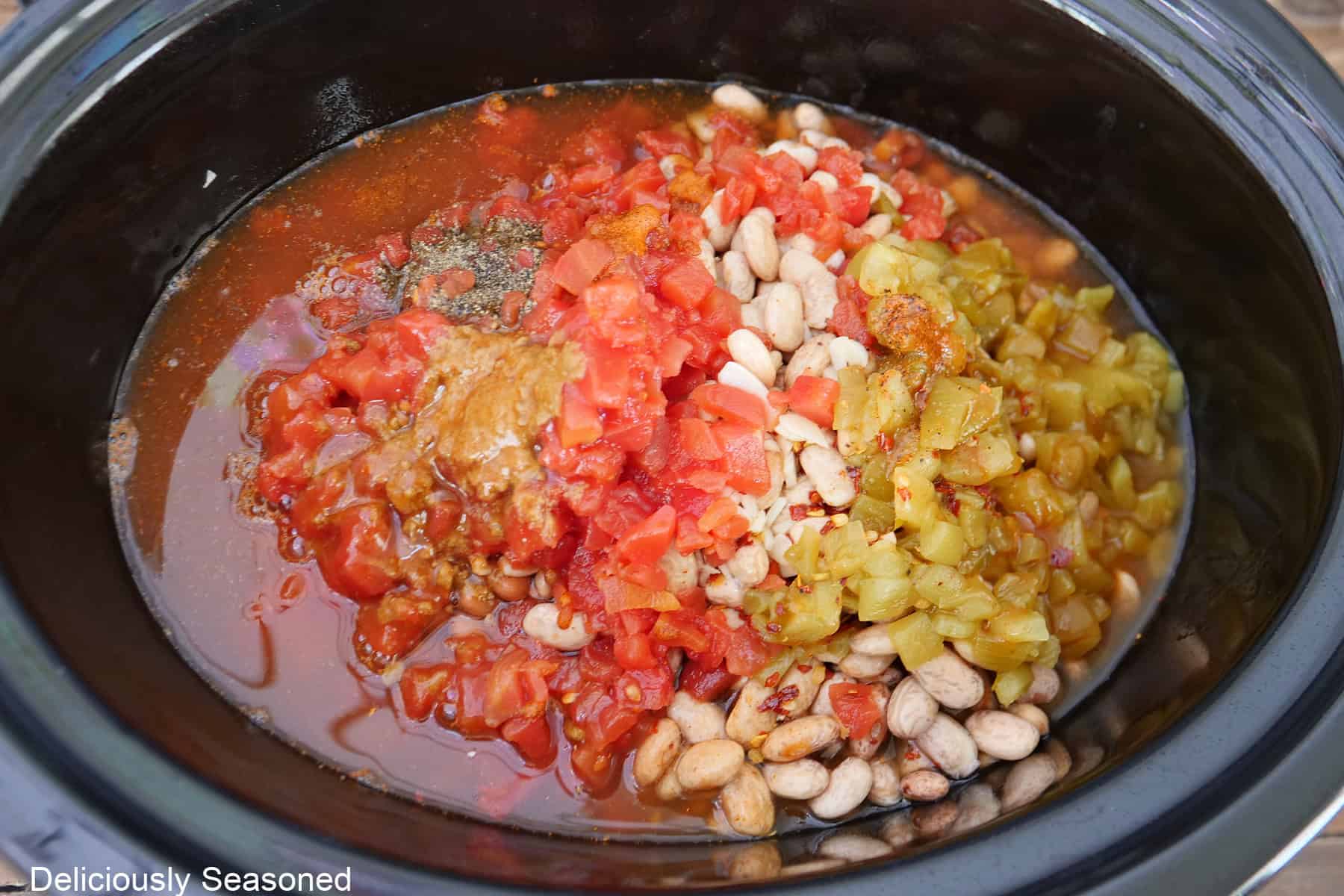 A crock pot with all the ingredients placed in it to make crock pot spicy beans before being stirred together.