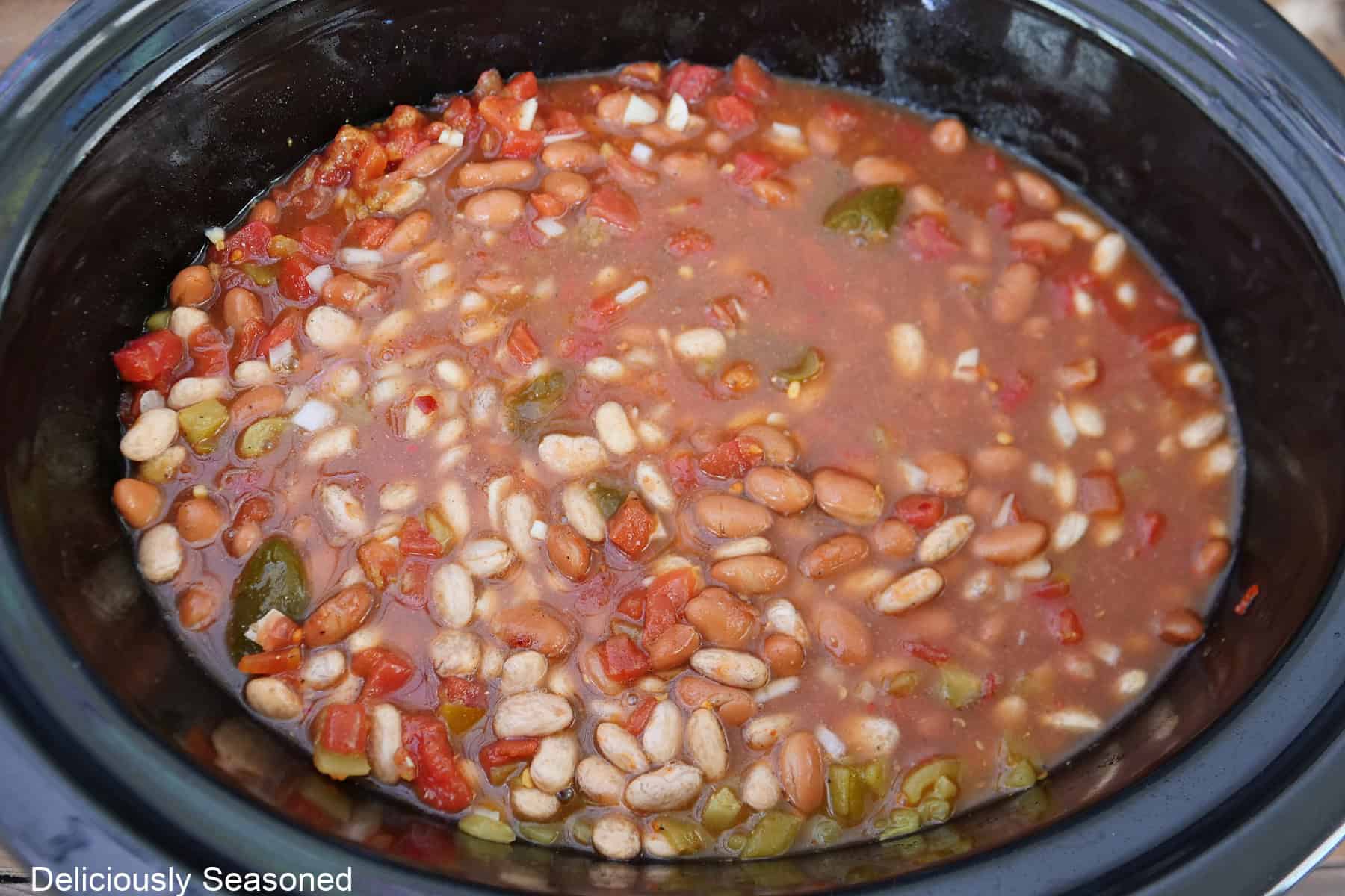 A crock pot with all the ingredients placed in it to make crock pot spicy beans.