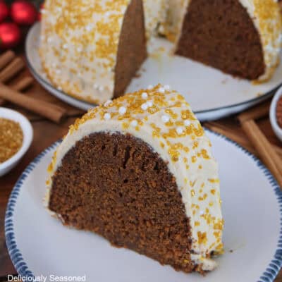 A slice of gingerbread bundt cake covered with molasses frosting and candy sprinkles on a white plate with blue trim .