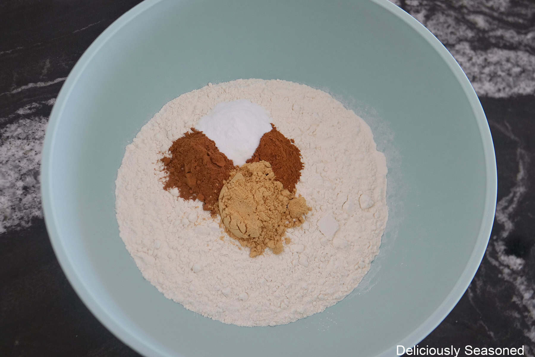 A light blue bowl with the dry gingerbread cake batter ingredients in it.