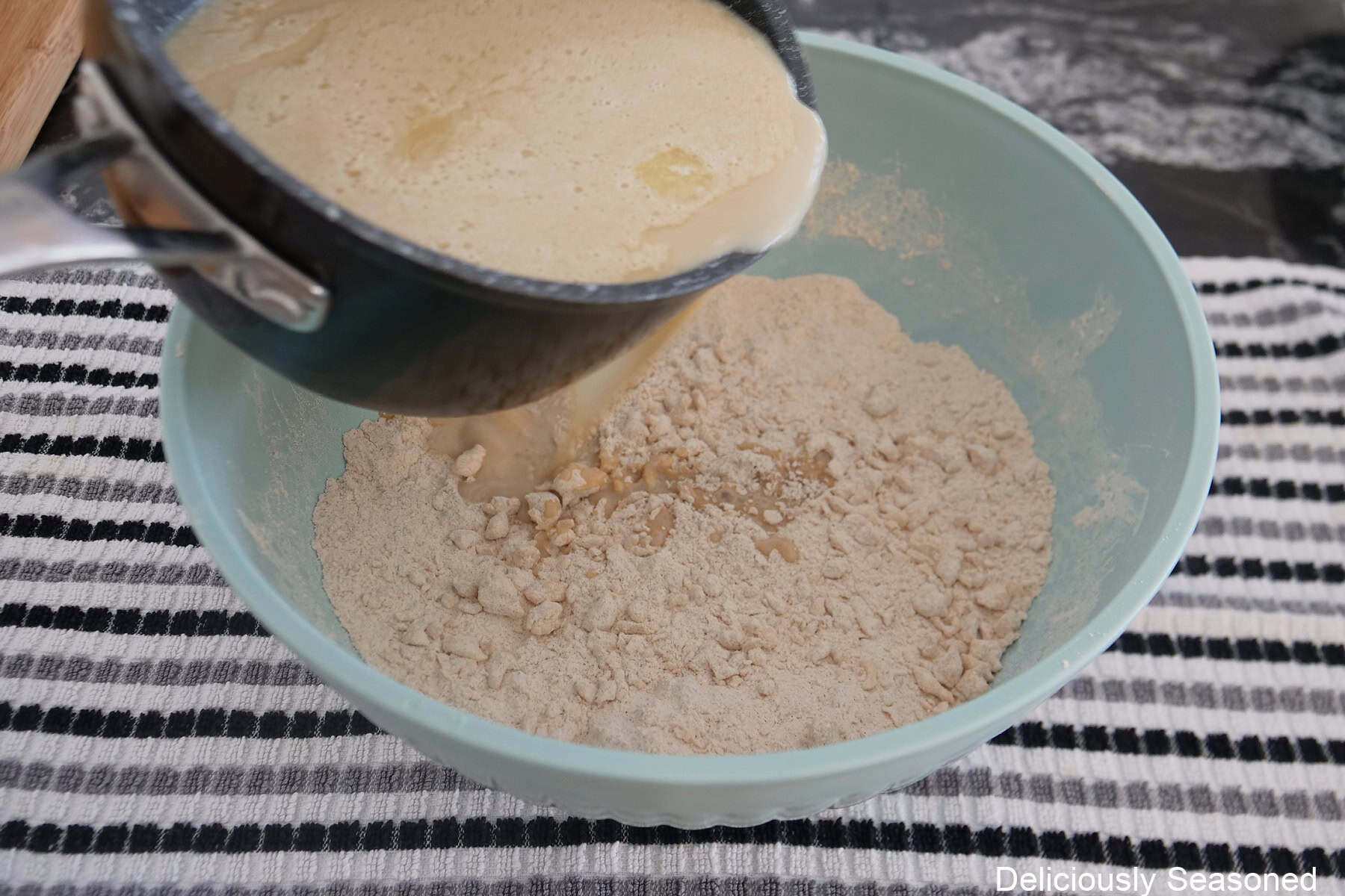 A saucepan pouring the wet gingerbread cake batter into the dry ingredients.