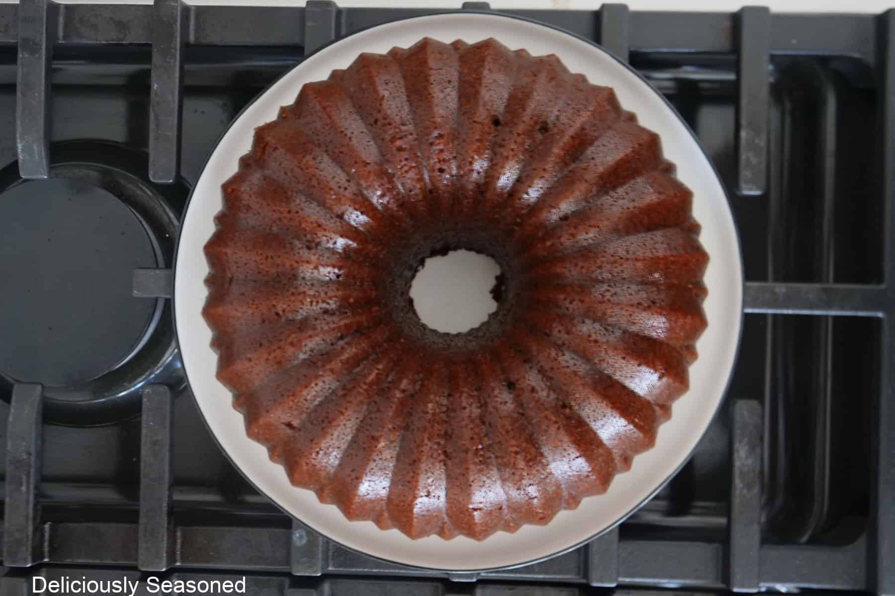 A white plate set on the stovetop with a baked gingerbread bundt cake on it.