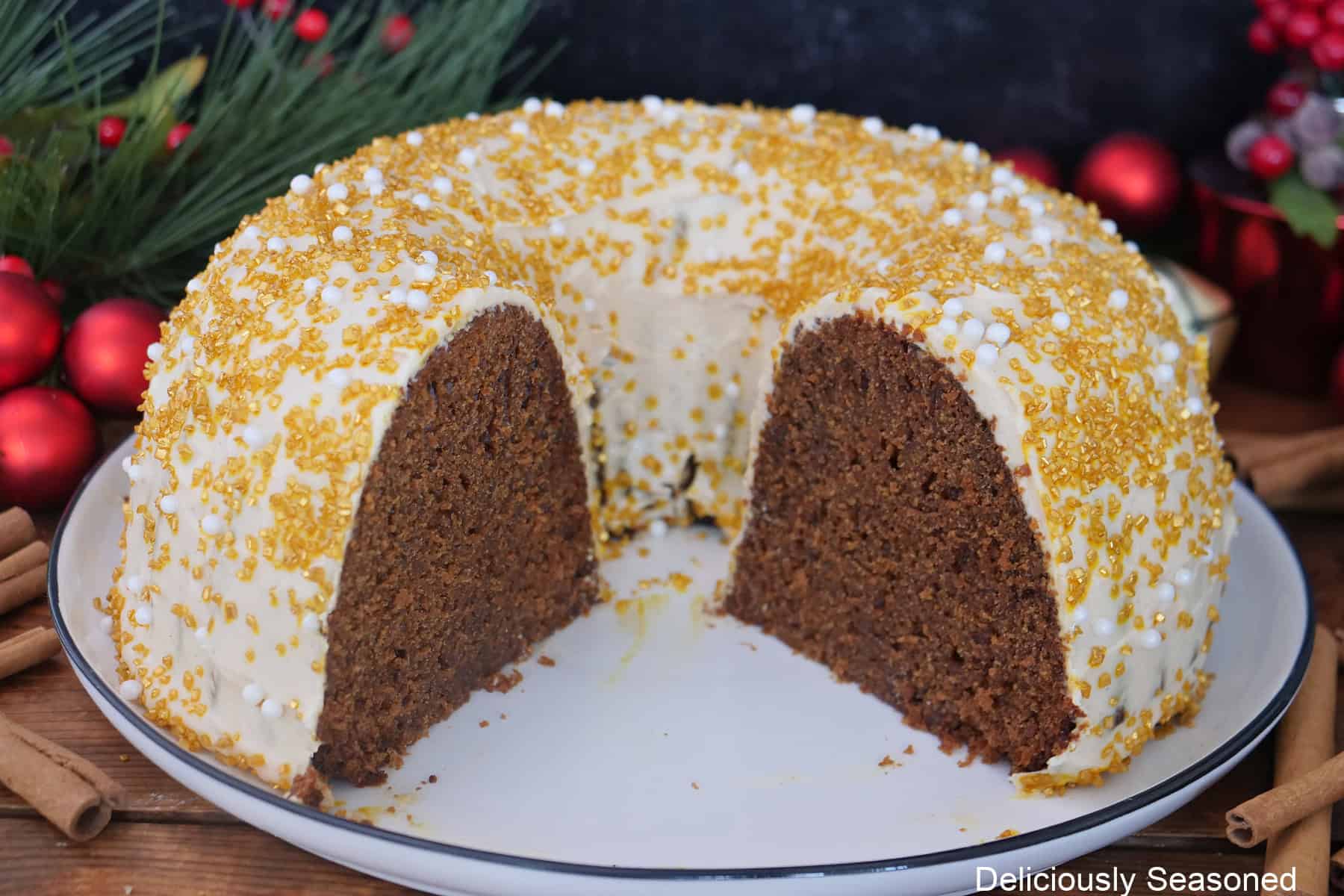A gingerbread bundt cake with molasses frosting on a white plate with molasses frosting and candy sprinkles over the cake, and a few pieces removed.