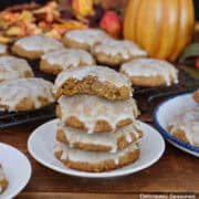Four pumpkin oatmeal cookies with maple icing stacked on a small white plate with a bite taken out of the top cookie.