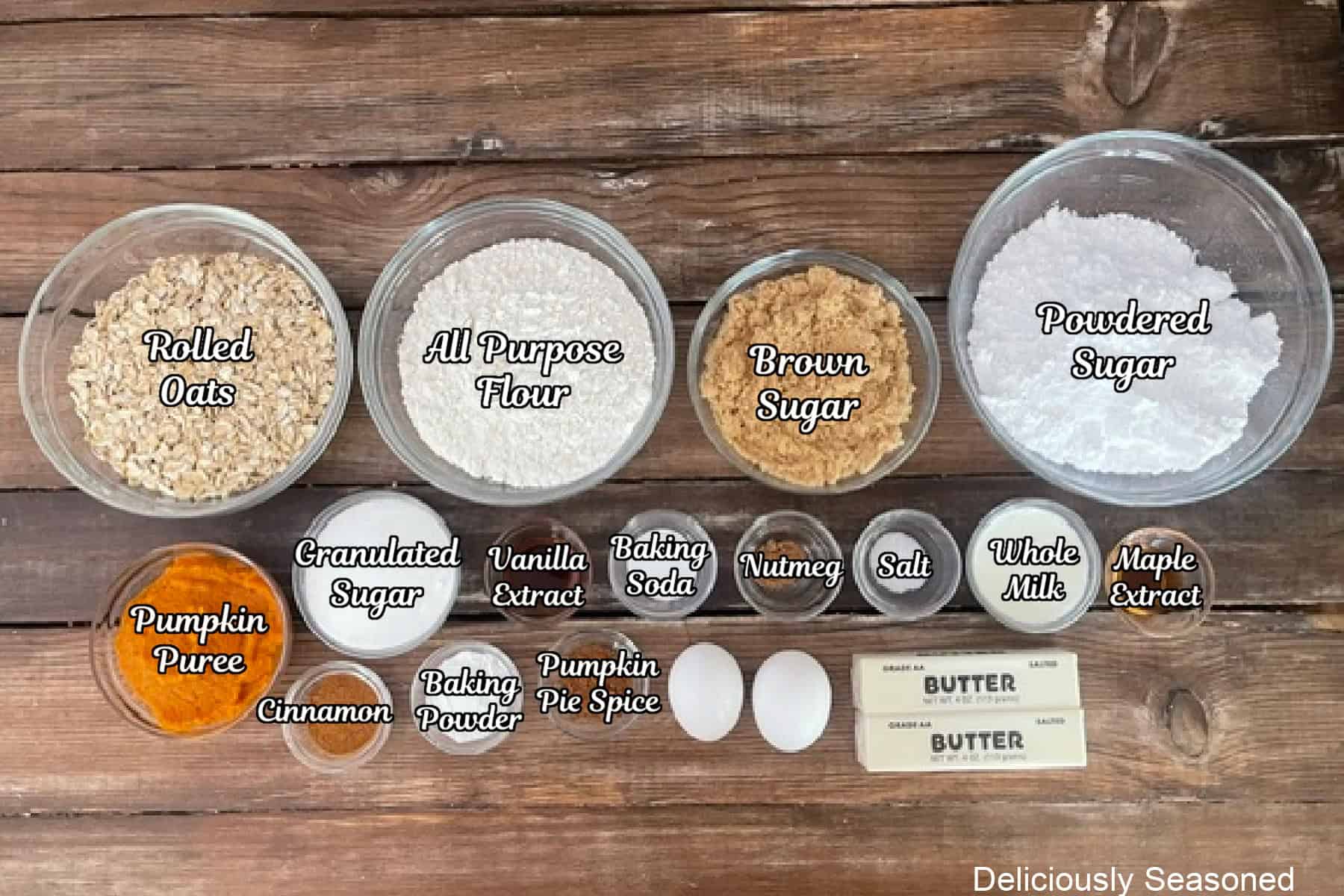 A rustic wood surface with all the ingredients placed on it to make maple iced pumpkin oatmeal cookies.