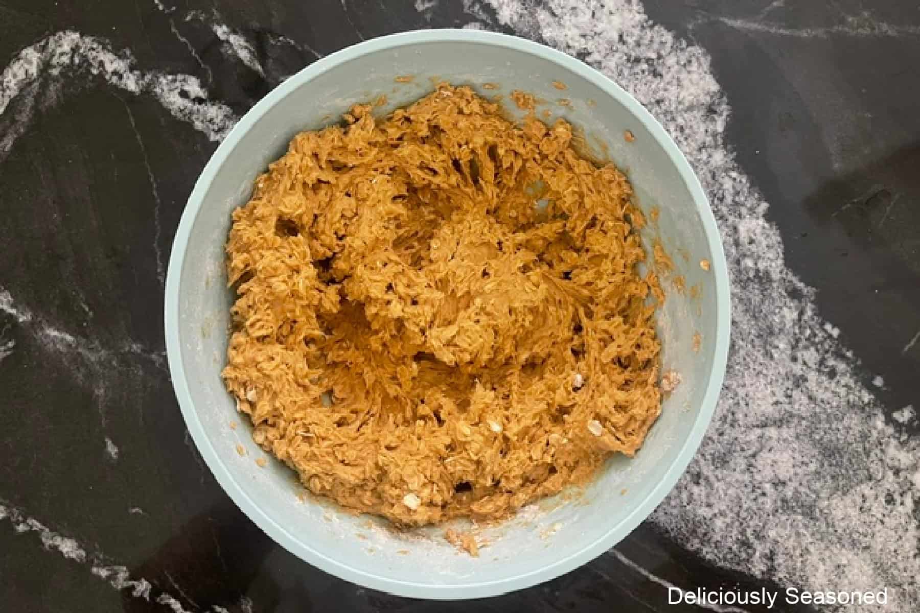 A light blue mixing bowl with pumpkin oatmeal cookie batter mixed together in it.