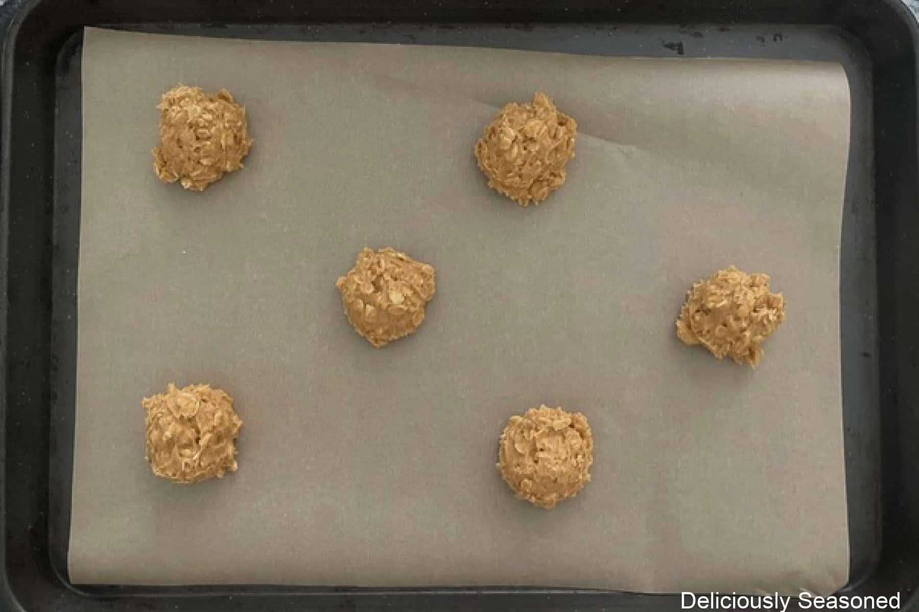 A parchment lined baking sheet with six pumpkin oatmeal cookie dough balls on it before being baked.