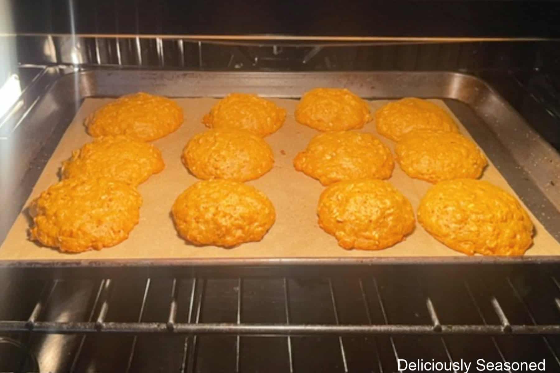 A baking sheet in the oven with a dozen pumpkin oatmeal cookies baking on it in the oven.