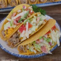 A white plate with blue trim with three pork tacos on it.