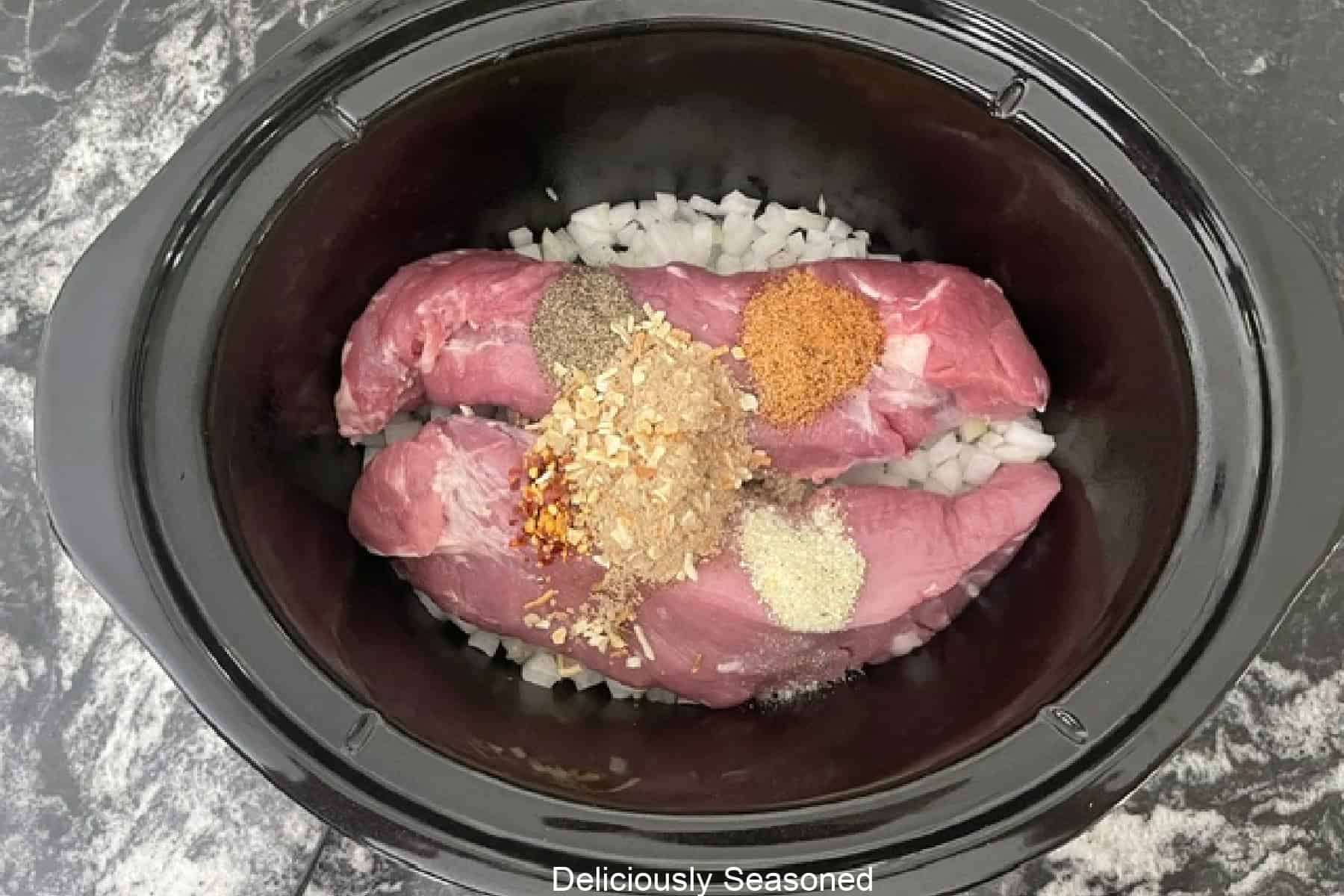A crock pot with a pork tenderloin and seasonings in it.