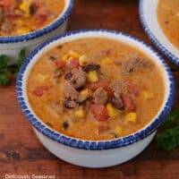 A wood surface with a white bowl with blue trim filled with a serving of southwest taco soup.