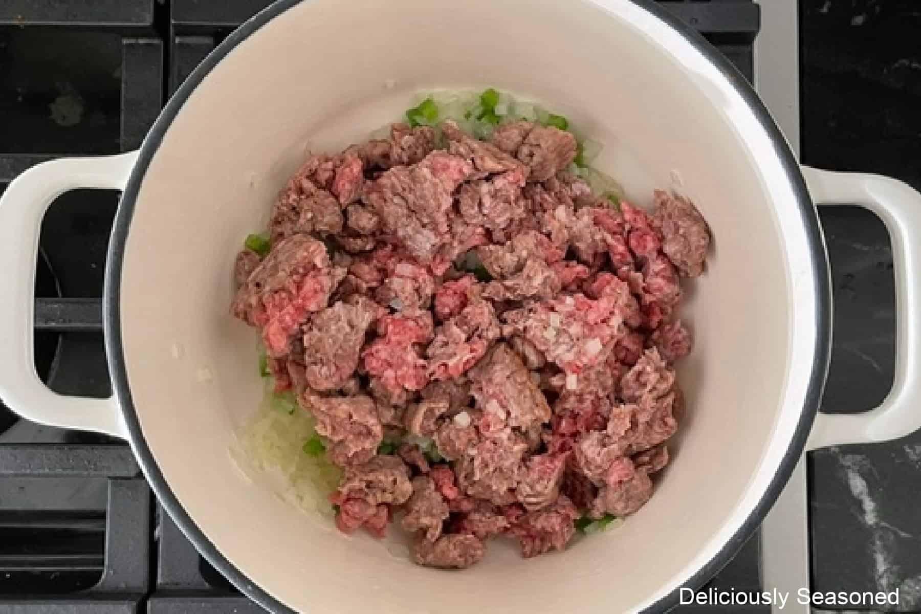 A white cast-iron skillet with ground beef added to onions and jalapenos.