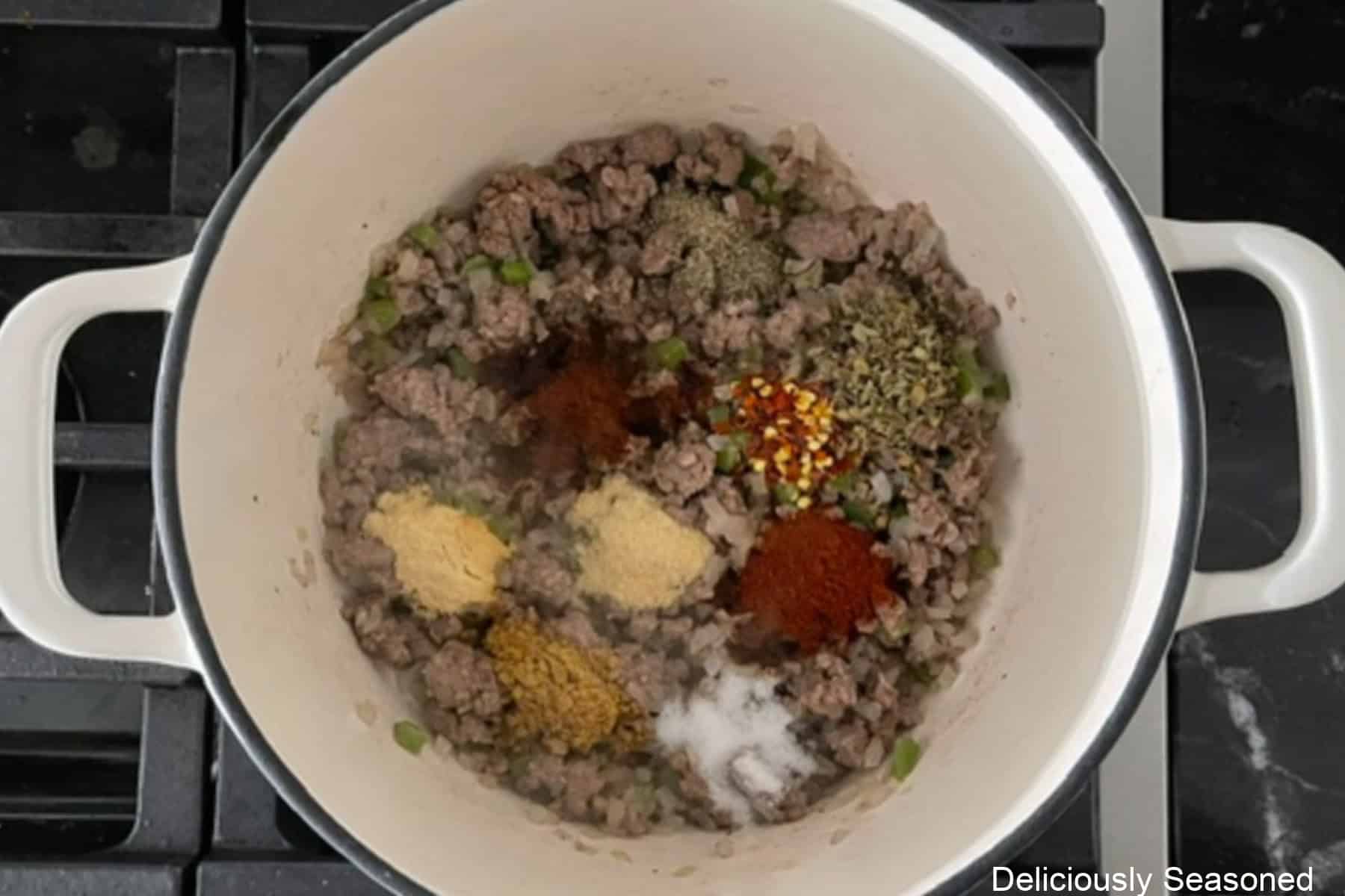 A white cast-iron skillet with seasonings added to cooked ground beef, onions, and jalapenos.