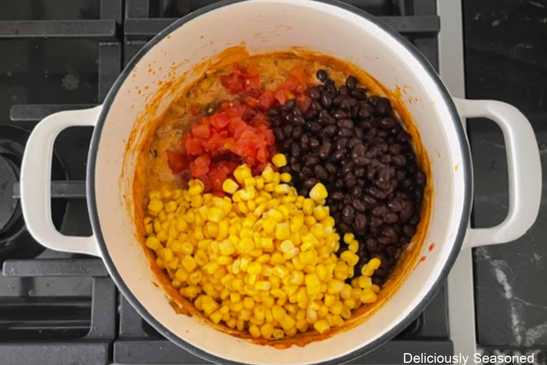 A white cast-iron skillet with corn, black beans, and tomatoes added to a ground beef mixture.